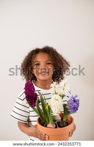 A smiling African American girl with bouncy curls presents a pot of vibrant hyacinths, a heartfelt Mother's Day gift symbolizing gratitude and love. High quality photo