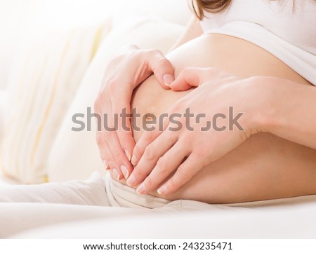 Pregnant Woman holding her hands in a heart shape on her baby bump. Pregnant Belly with fingers Heart symbol. Maternity concept. Baby Shower. Motherhood 