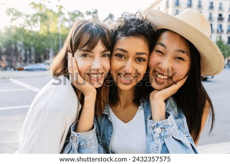 Cute portrait of three young best female friends looking at camera standing at city street during summer holidays. Friendship concept.