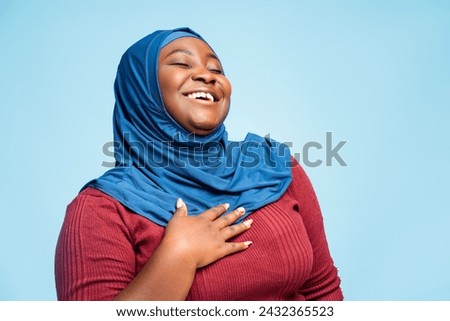 Beautiful, smiling arabic woman wearing stylish traditional hijab looking away isolated on blue background. Happy African American religious student posing in studio. Fashion concept