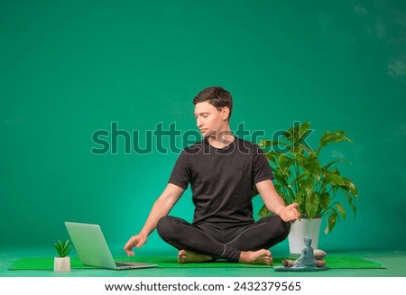 a man does yoga remotely. a man with a laptop in a yoga pose isolated on a green background