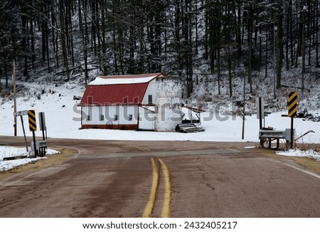 an old red and white barn at the end of a curve of a rural highway in winter