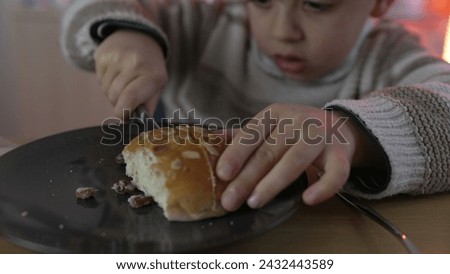 Young Boy Skillfully Slices Bread for Snack, Carb Food Preparation and takes a bite of carb rich food. 5 year old child snacking Royalty-Free Stock Photo #2432443589