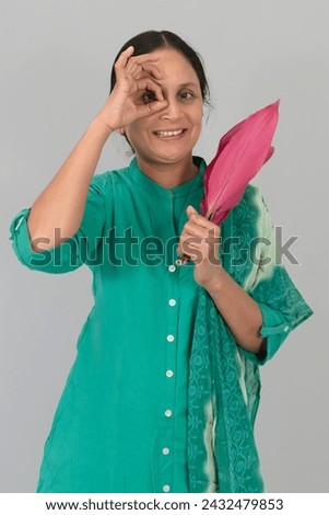 A young woman holding tree leaves in her left hand with a right hand near-eye with an "ok" gesture, the celebration of Happy Women's Day. Isolated on a Grey Background