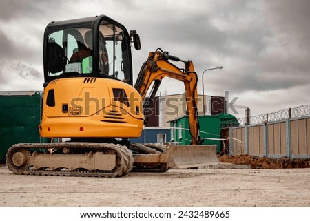 A mini excavator rams the ground with a vibrating plate. Laying of underground sewer pipes and communications during construction. soil compaction. Earthworks, excavation Royalty-Free Stock Photo #2432489665