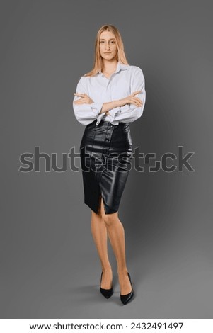 Young blonde woman in white shirt and leather pencil skirt with folded arms Royalty-Free Stock Photo #2432491497