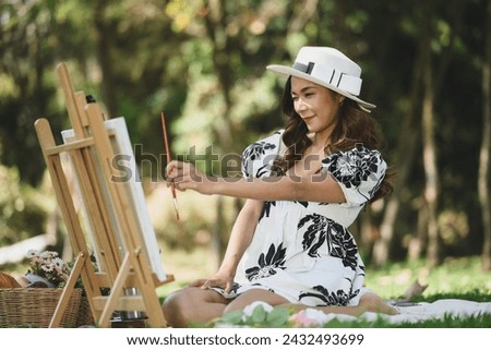 Attractive young woman in casual dressed painting picture on a canvas during a picnic in the park