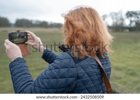 Woman tourist seen using her smart phone to take a landscape image of a wildlife park in the Britain.