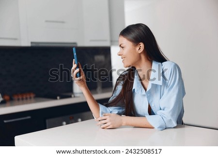 Woman sitting at kitchen table checking her cell phone and looking at screen with concentration and interest