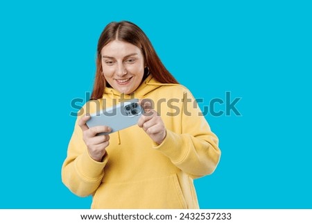 Close up portrait of a Happy 30s woman playing games with a smart phone isolated on a blue background