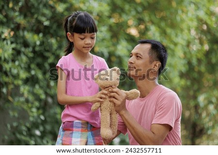 A father is giving a brown teddy bear to his daughter on the occasion of her being a good girl. It is a picture of a cute family with smiles. and shows the love and care of a father for his daughter.