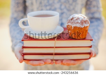woman holding hot cup of tea, homemade cupcake with stacked books