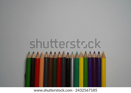A row of sharpened colored pencils arranged in a line against a clean, white background. The pencils boast a wide variety of bright colors, including red, yellow, blue, green, and purple. This image i