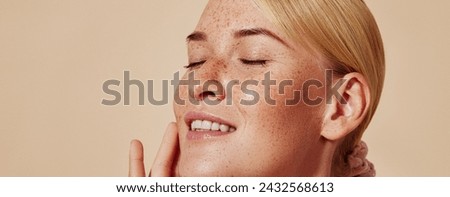 Side view of smiling blond woman with freckles touching her face. Close-up studio shot of young positive female with closed eyes against pastel background. Royalty-Free Stock Photo #2432568613