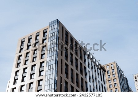 A modern tower block with a sleek facade rises against a clear blue sky, showcasing urban design and composite materials in a commercial building Royalty-Free Stock Photo #2432577185
