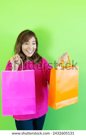 photograph of cheerful and beautiful woman looking at her happy colorful shopping bags. on green background