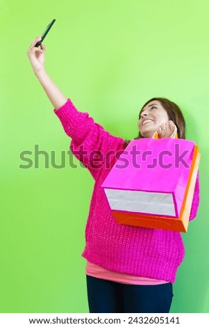 photograph young girl taking a selfie with shopping bags smiling happily. green background