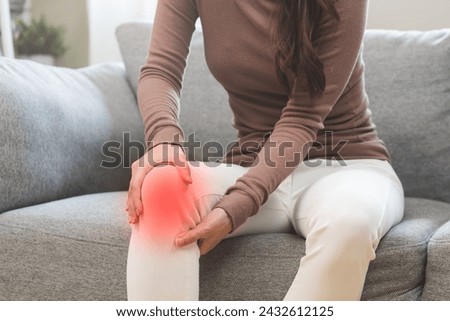Health care of knee pain concept, close up hand of woman arthritis sitting joint ache, sore cramp or sprain tendon in leg on sofa at home. Osteoarthritis chronic disease of body problem from trauma. Royalty-Free Stock Photo #2432612125