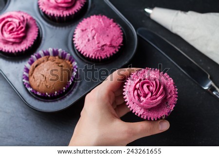 Cupcake decoration - chocolate and blackcurrant buttercream cupcakes on different stages, knife, pastry bag on dark stone background