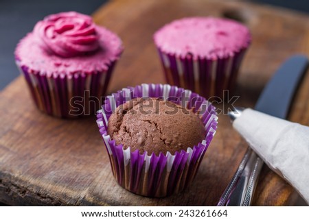 Cupcake decoration - chocolate and blackcurrant buttercream cupcakes on different stages, knife, pastry bag on wood background