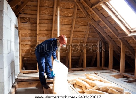 Roof insulation. A worker puts glass wool insulation in the attic. Royalty-Free Stock Photo #2432620017