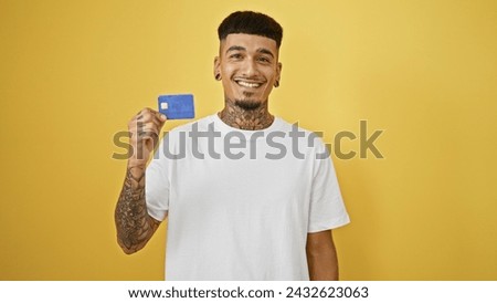 Cheerful young hispanic man exuding confidence, smiling with credit card against a yellow isolated background