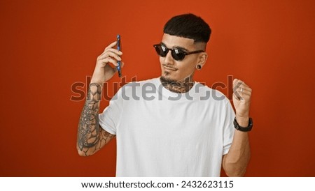 Cheerful young latino man dancing with joy while listening to catchy tunes on his phone, isolated over a vibrant red background