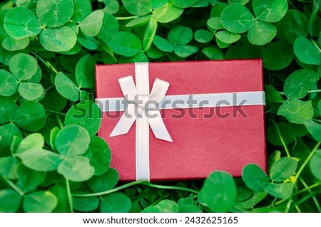 Red gift box on green clover leaves background. St.Patrick's Day