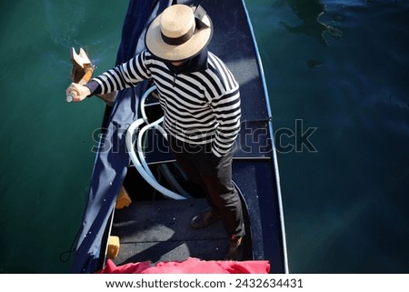 Venetian Gondolier with blue and white striped shirt while rowing the Gondola in the Grand Canal in Venice in Italy Royalty-Free Stock Photo #2432634431