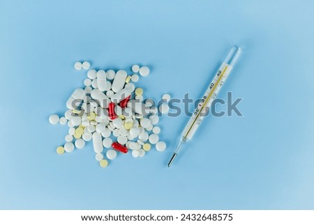 a scattering of different colors and shapes of tablets on a blue paper background and a thermometer with a temperature reading of 37 degrees