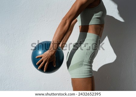 a girl with a sports outfit statically holds a mini fitness ball in her hands. close-up views of a sports girl with a ball in her hands. concept of sport and healthy lifestyle