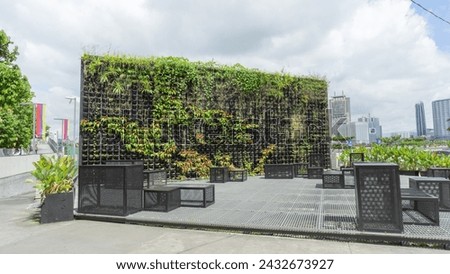 Place to sit and relax See the scenery Decorated with a vertical garden. There is a rectangular chair. For sitting and resting It's a public area. The atmosphere behind is a large tall building. 