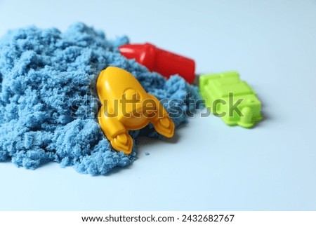 Bright kinetic sand and plastic toys on light blue background, space for text
