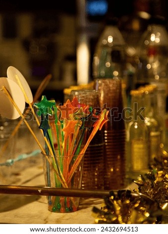 Vibrant cocktail stirrers in star shapes, glasses and golden tinsel on a bar counter, conveying a festive, celebratory mood Royalty-Free Stock Photo #2432694513