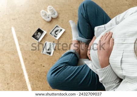 top view of a pregnant woman's belly. Ultrasound image of a pregnant woman. expecting a child. close-up of the belly of a pregnant woman sitting on the floor inside the house Royalty-Free Stock Photo #2432709037