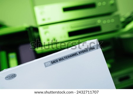The package of a new SACD featuring hi-def jazz music is showcased against a vivid green background, with a defocused hi-fi audiophile system in the backdrop Royalty-Free Stock Photo #2432711707