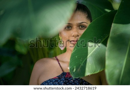 face of a young latin woman looking at the camera in the middle of the leaves of the trees 