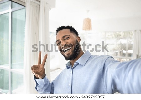 Happy joyful African American guy showing victory winner fingers sign and toothy smile, looking at camera, making peace hand gesture, taking selfie portrait, enjoying success, laughing