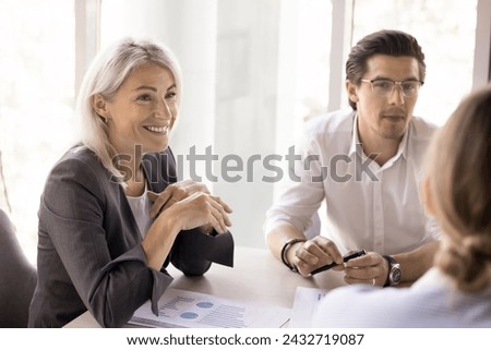 Mature smiling businesslady take part in meeting in office with colleagues, business partners, staff members to share ideas, express opinion, consider joint project, strategy discussion in boardroom Royalty-Free Stock Photo #2432719087