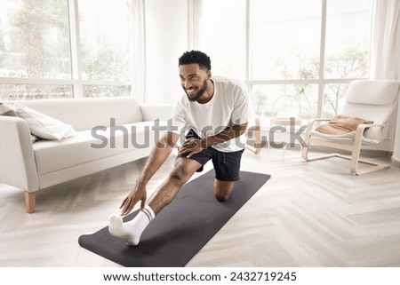 Positive attractive athletic young African man exercising on yoga mat at home, stretching hip, back muscles, bending forward to leg, training body, caring for wellness, flexibility