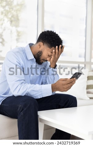 Tired frustrated young African man having problems with mobile phone, bad connection, online communication failure, application error, touching head with closed eyes Royalty-Free Stock Photo #2432719369