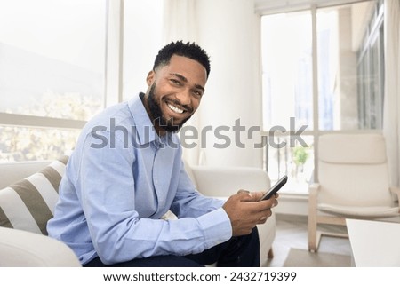 Happy young African American man holding smartphone, looking at camera with toothy smile. Portrait of positive customer satisfied with mobile phone online service, application