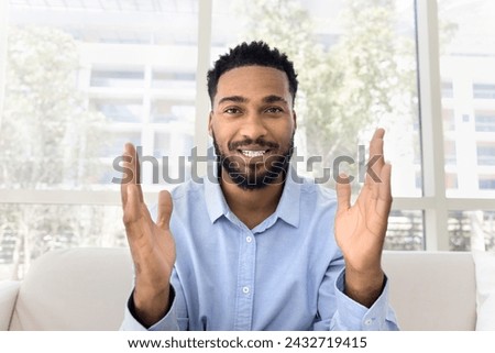 Positive attractive African influencer guy speaking at camera, making hand gesture, showing length, dimension, holding copy space for advertising header. Video call screen head shot Royalty-Free Stock Photo #2432719415