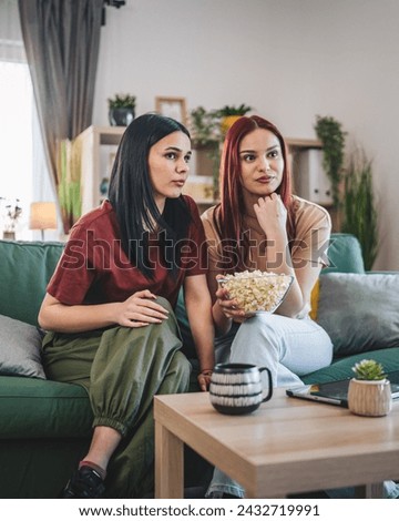 two women caucasian teenage friends or sisters watch movie tv series at home sit on sofa bed with popcorn