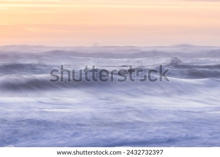 The ocean is rough and choppy, with waves crashing against the shore. The sky is a mix of pink and orange hues, creating a serene and calming atmosphere