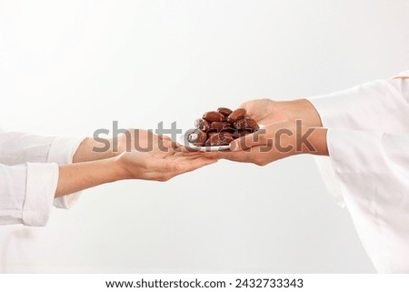 Concept Giving or Charity during Ramadhan Holy Month, Female Muslim Hand Over A Plate of Dates Fruit Kurma to Other. Ifthar and Ramadan Kareem Concept.  Royalty-Free Stock Photo #2432733343