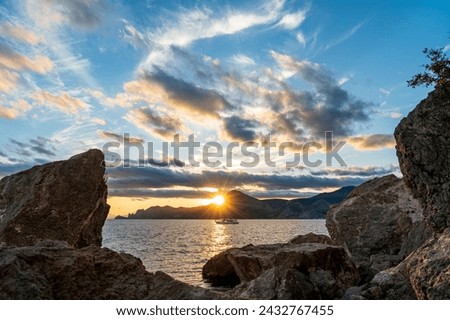 Sudak, Crimea. Sunset over the waters of the Black Sea. The ship against the backdrop of the sun. Rocks and backlight. Contrasting and bright sky with clouds Royalty-Free Stock Photo #2432767455