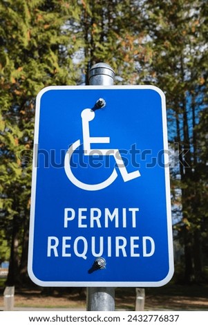 Handicap parking sign with trees background. Handicapped parking spot. Blue handicapped sign. Disabled parking permit sign on pole. Reserved parking lot for mobility or disable people