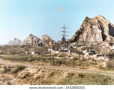 mountains with railway track and electric poles house wires with blue sky.
photo contain exposure grain and highlights.