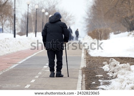 Elderly man with walking cane on a winter street. Concept of limping, old age, snow weather Royalty-Free Stock Photo #2432823065